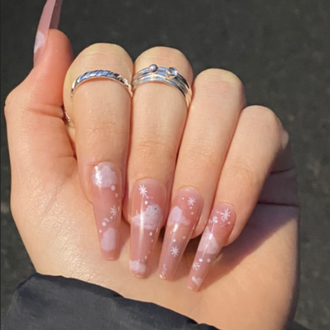 false press on nails that are pink with white airbrush designs of clouds and stars on them in a long coffin shape